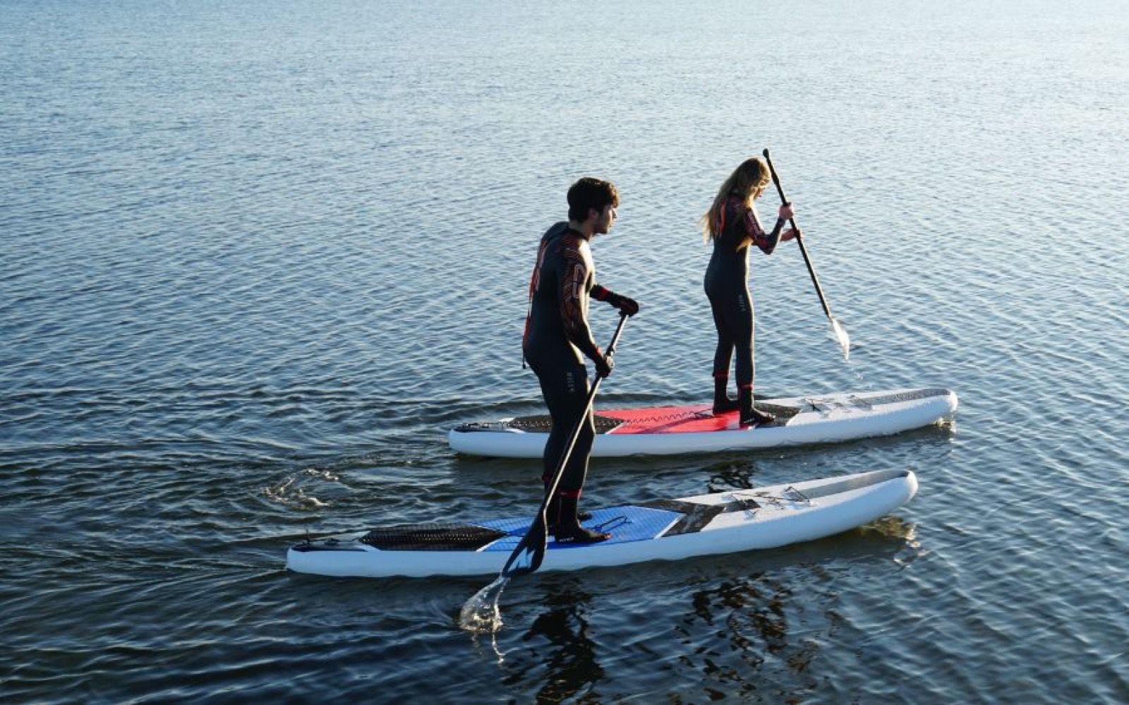 To personer står på paddleboards på havnen