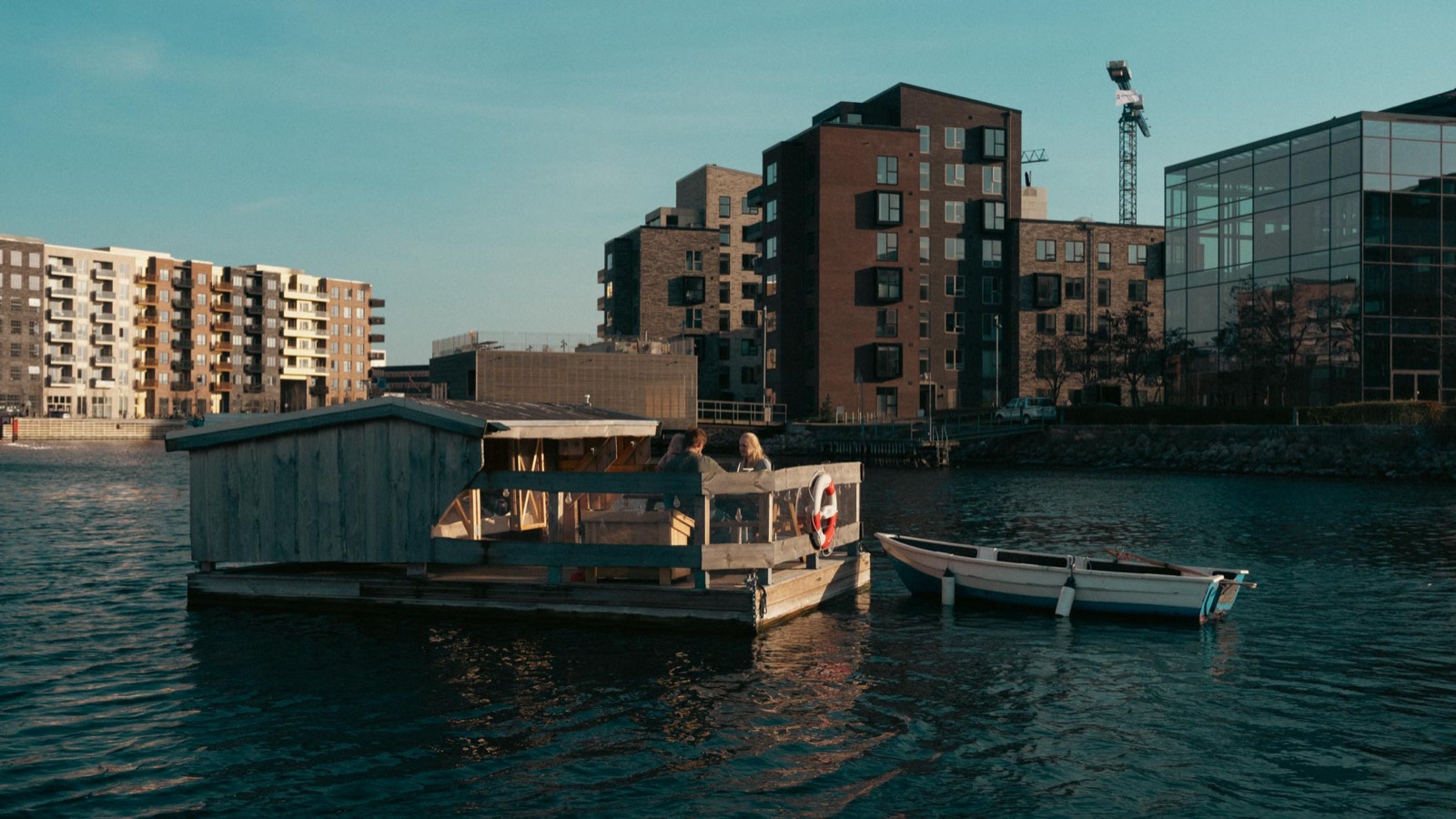 Blue Raft forankret i havnen i aftensol med robåden ved siden af