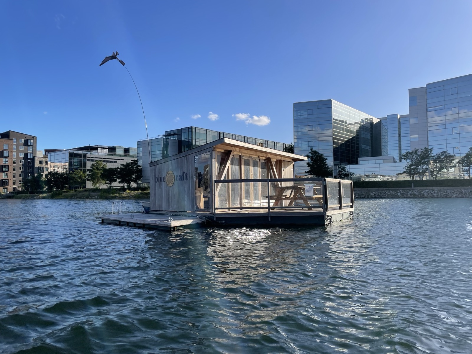 Blue Raft, en flydende hytte af træ og glas, ligger i havnen under en blå himmel
