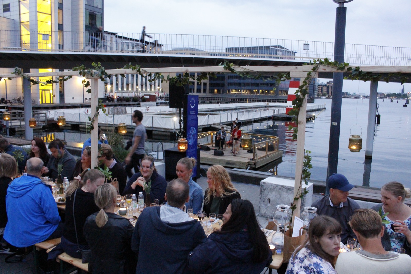 Gæster spiser ved lange borde på kajen til et havne-event