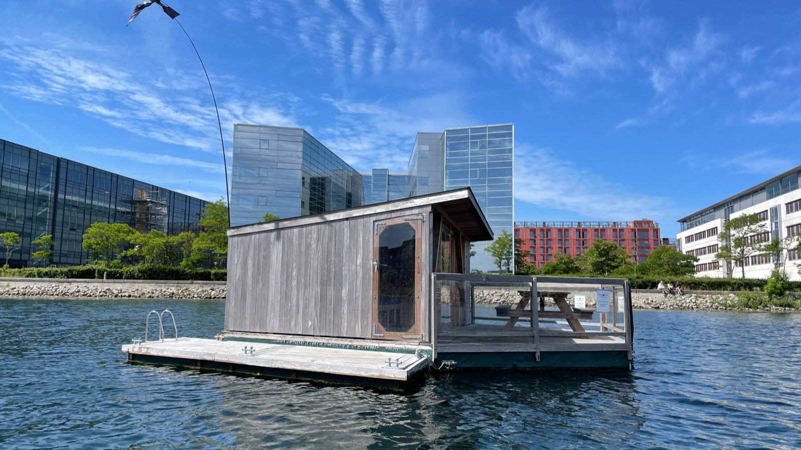 Blue Raft 2, en flydende hytte på en tømmerflåde, i havnen foran moderne bygninger