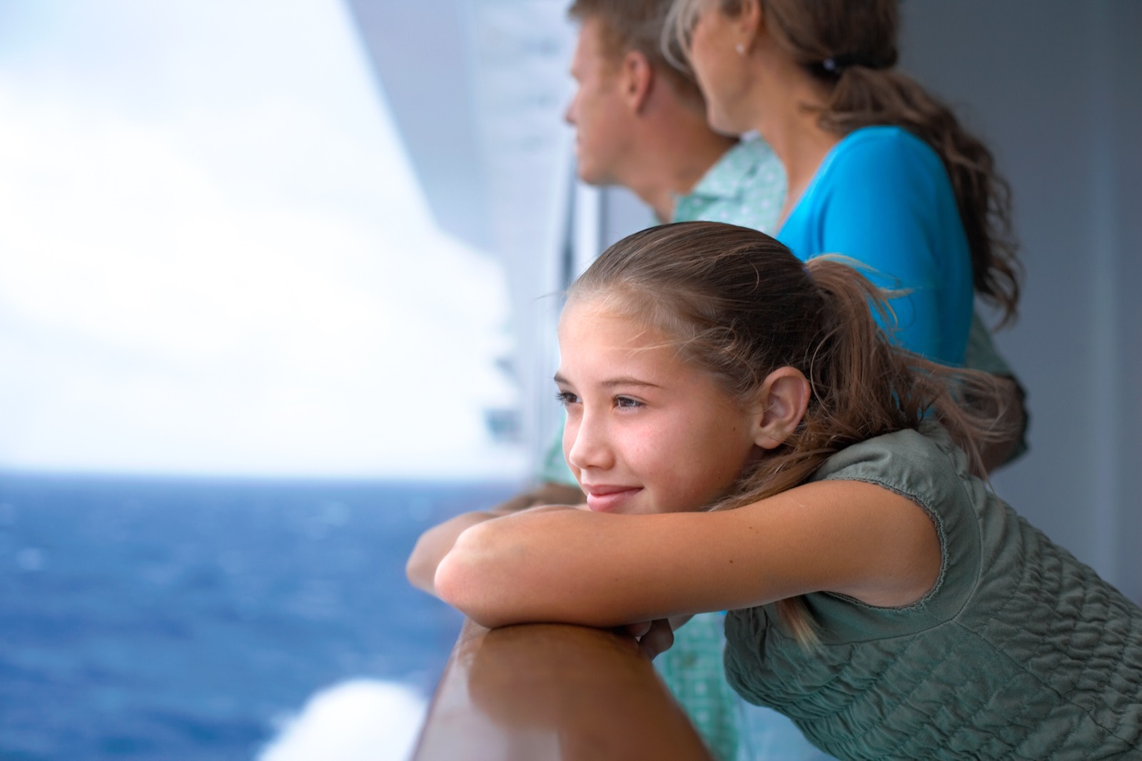 Ein Mädchen und seine Familie lehnen an der Reling und blicken aufs Meer