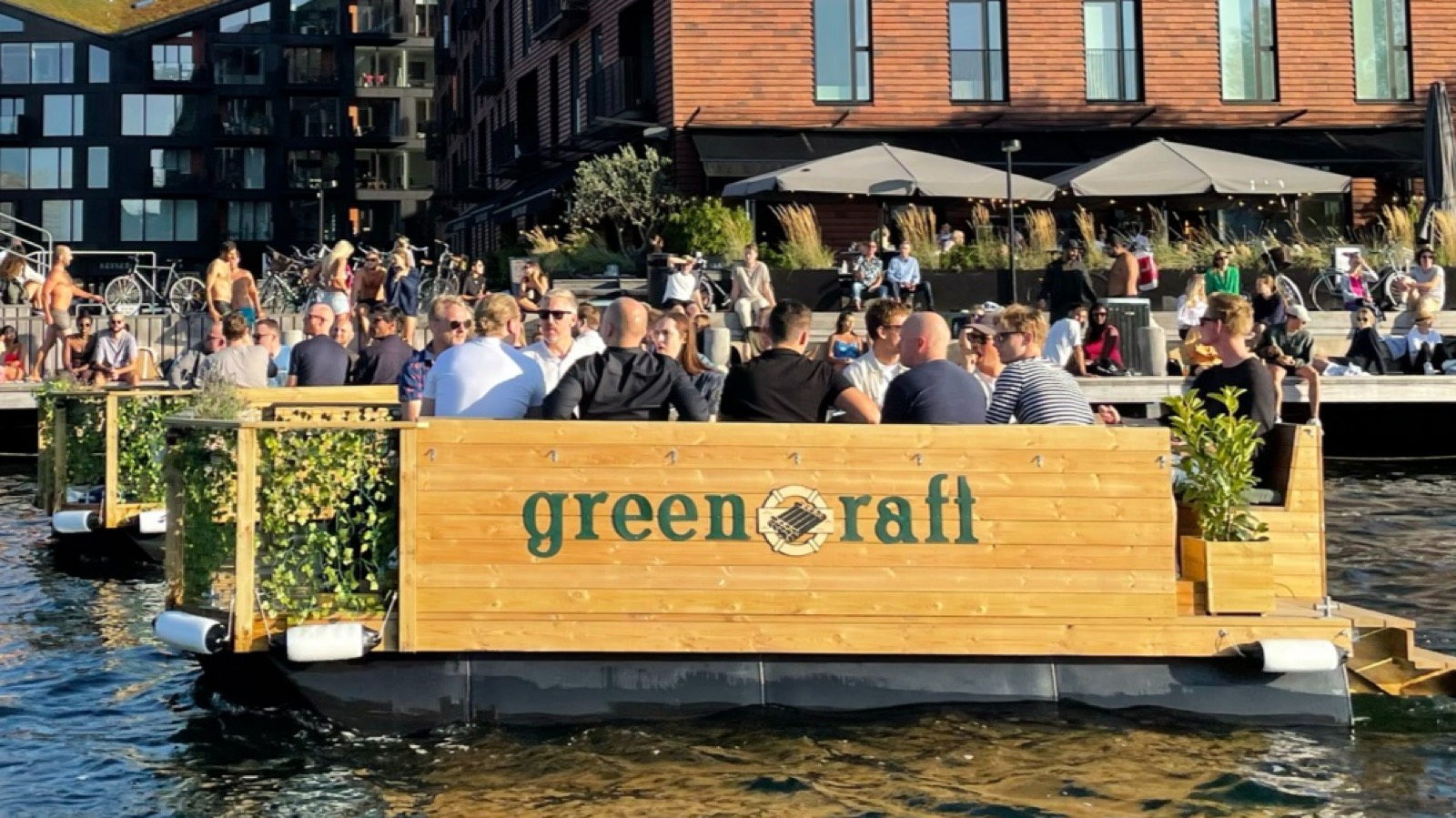 En Green Raft fuld af gæster ved kajen foran en travl udendørsbar